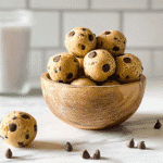 edible cookie dough bites with chocolate chips in a wooden bowl on a marble counter.