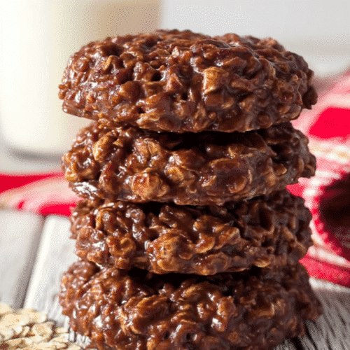 Stack of rich, chewy no bake cookies made with powdered milk, oats, and cocoa on a rustic wooden table
