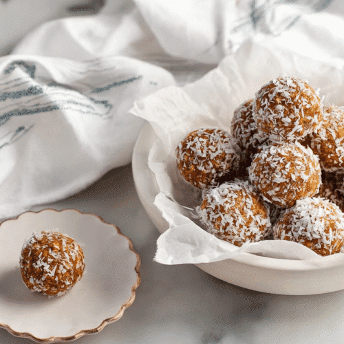 Carrot cake energy balls rolled in shredded coconut served in a white bowl on a marble countertop
