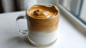 Cloud coffee recipe in a glass mug with whipped coffee foam over milk near a window