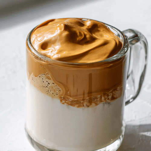 Cloud coffee recipe with whipped golden foam over milk in a glass mug on a white surface