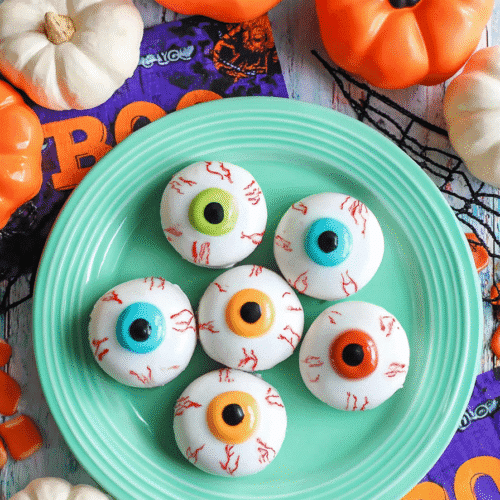 Halloween-themed no-bake cookies decorated like eyeballs on a green plate with pumpkins and spooky decor