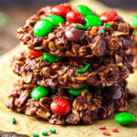 Holiday no bake cookies with chocolate, oats, and festive red and green M&M candies stacked on parchment paper.