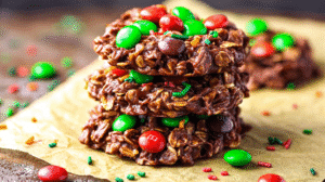 Holiday no bake cookies with chocolate, oats, and festive red and green M&M candies stacked on parchment paper.