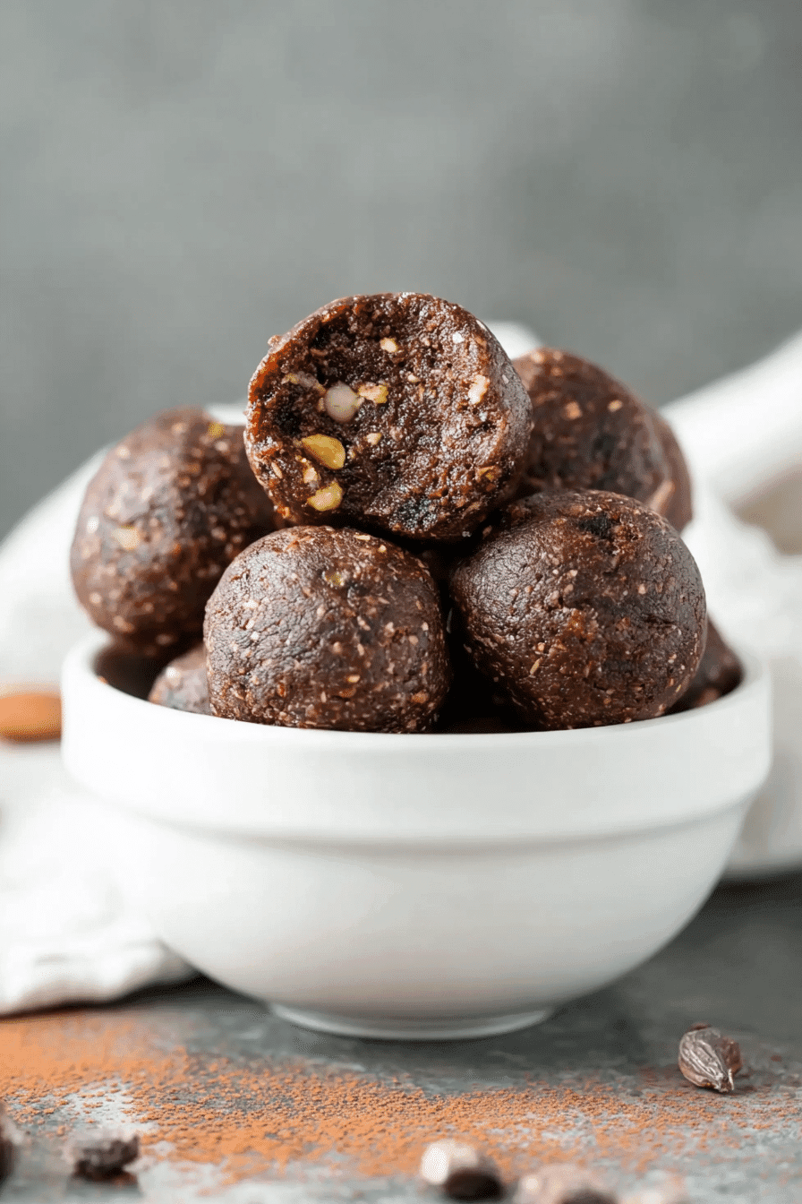 Keto energy balls with nuts and chocolate stacked in a white ceramic bowl.