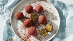 Superfood energy balls coated in cocoa powder with pistachio filling on a white plate