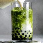 A tall glass of matcha bubble tea with dark tapioca pearls at the bottom and creamy milk swirling into vibrant green tea.