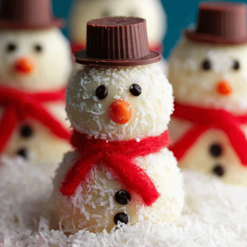 Snowman no bake cookies covered in coconut with candy faces and chocolate peanut butter cup hats.